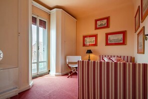 A room with a striped sofa, a chair, and a lamp. There are framed pictures on the wall. - Casa Golena (Venezia)