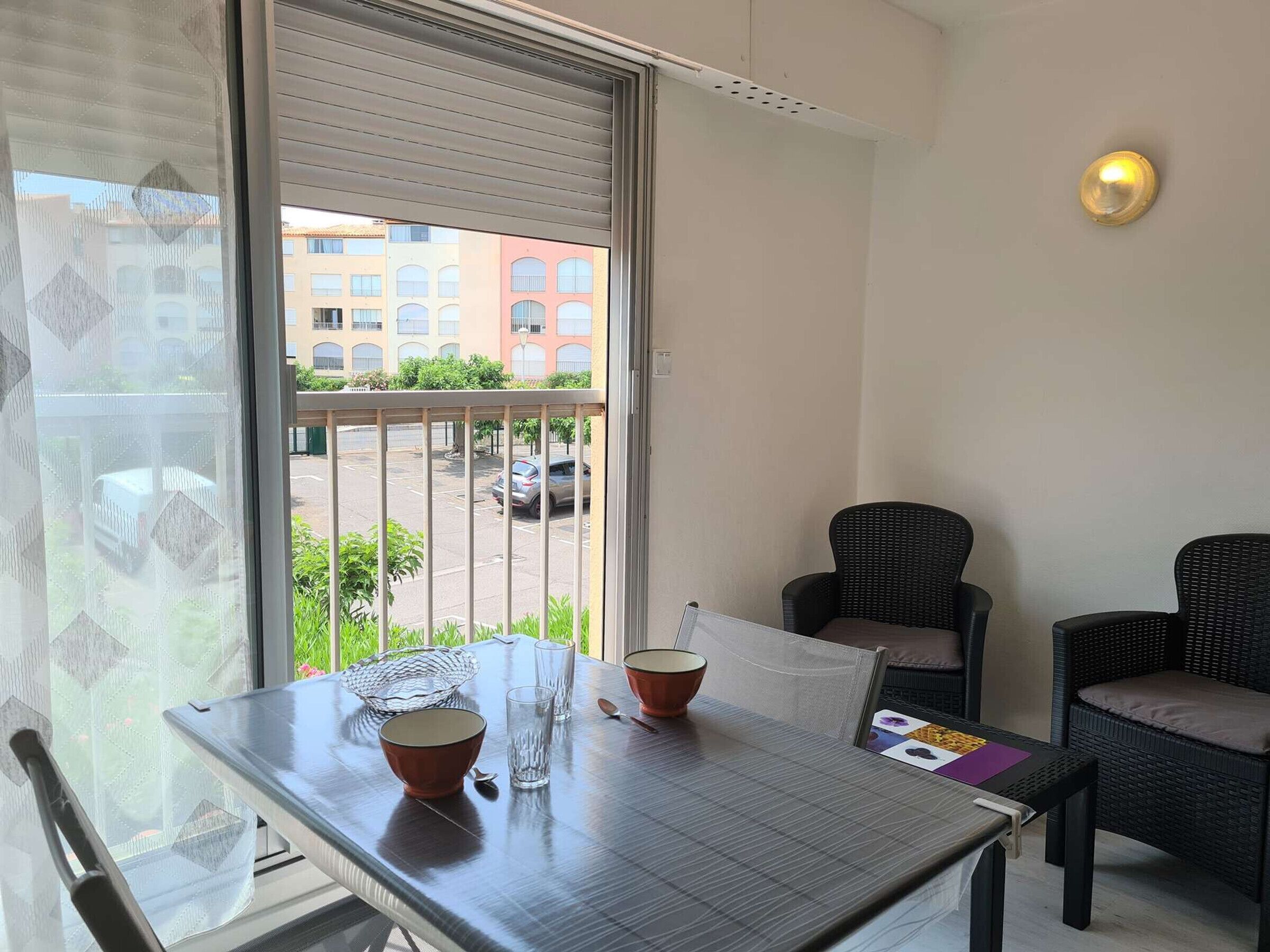 A balcony with a table, chairs, and a view of buildings and parked cars.