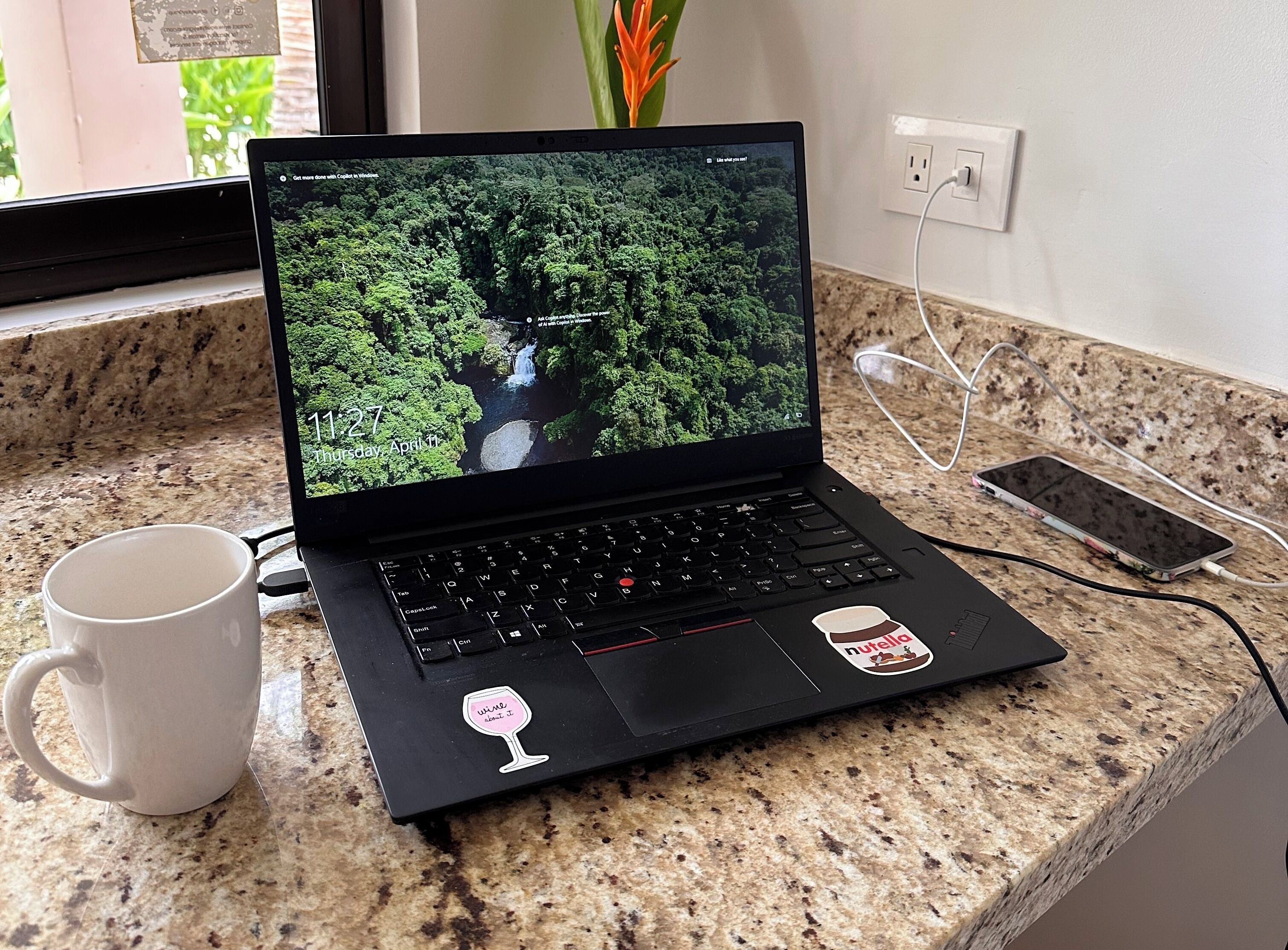 Una computadora portátil sobre una encimera de granito con una taza blanca a su lado.