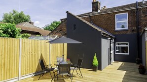 A patio area with a table and chairs, a wooden fence, and a house in the background.