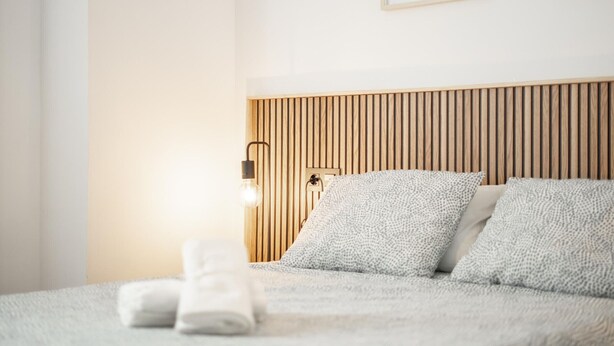 A neatly made bed with a wooden headboard, a wall-mounted light, and two framed pictures. - Oasis de Luxe au Cœur de Grenade: Appartement Moderne, Proche Alhambra, Wi-Fi Gratuit, 2 Chambres (Granada)