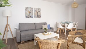 A modern living room with a grey sofa, white coffee table, wicker chairs, and a dining area with white chairs and a table. - Oasis de Luxe au Cœur de Grenade: Appartement Moderne, Proche Alhambra, Wi-Fi Gratuit, 2 Chambres (Granada)