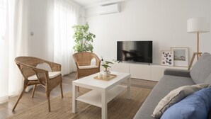 A modern living room with a white sofa, two wicker chairs, a coffee table, a flat-screen TV, and a floor lamp. - Oasis de Luxe au Cœur de Grenade: Appartement Moderne, Proche Alhambra, Wi-Fi Gratuit, 2 Chambres (Granada)