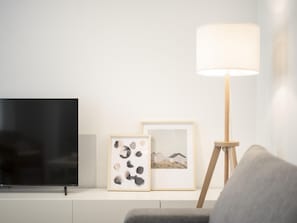 A modern living room with a flat-screen TV, two framed artworks, a floor lamp, and a grey sofa.