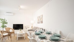 A modern living room with a TV, sofa, dining table set, and a small plant. - Oasis de Luxe au Cœur de Grenade: Appartement Moderne, Proche Alhambra, Wi-Fi Gratuit, 2 Chambres (Granada)
