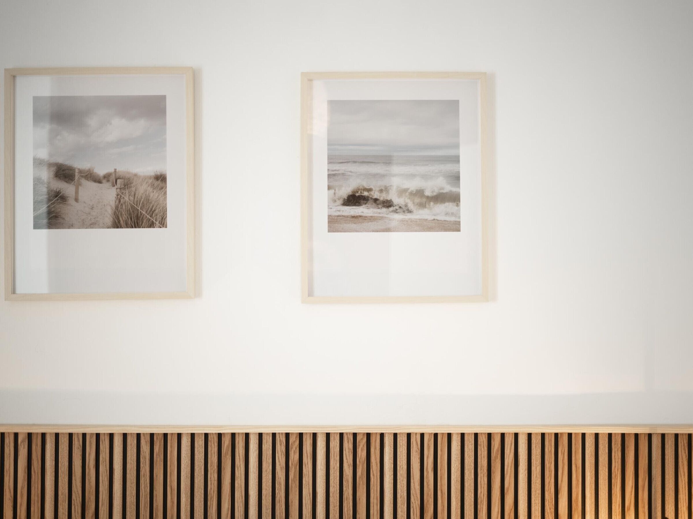 Two framed photographs of beach scenes on a white wall.