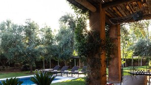 Une terrasse extérieure avec une piscine, des chaises longues et une table agrémentée d’un vase de fleurs.