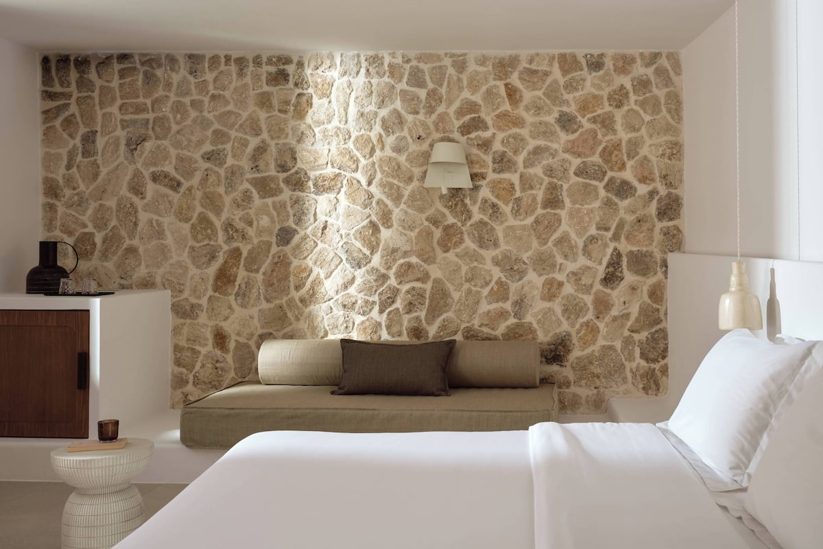 A bedroom with a stone wall, a bed, a sofa, a small table, and a cabinet.