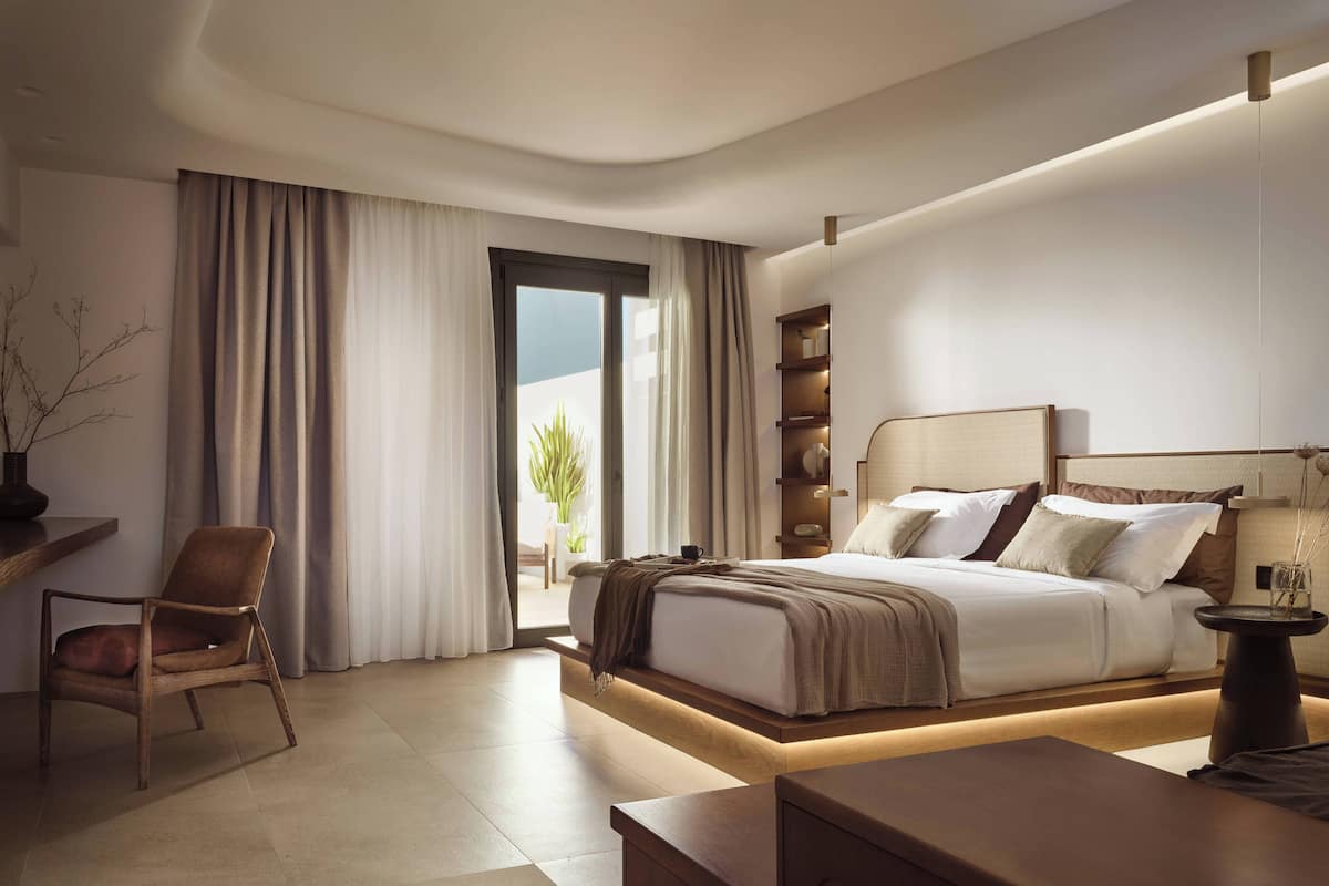 A modern hotel room with a large bed, a desk, a chair, and a view of the outdoors.