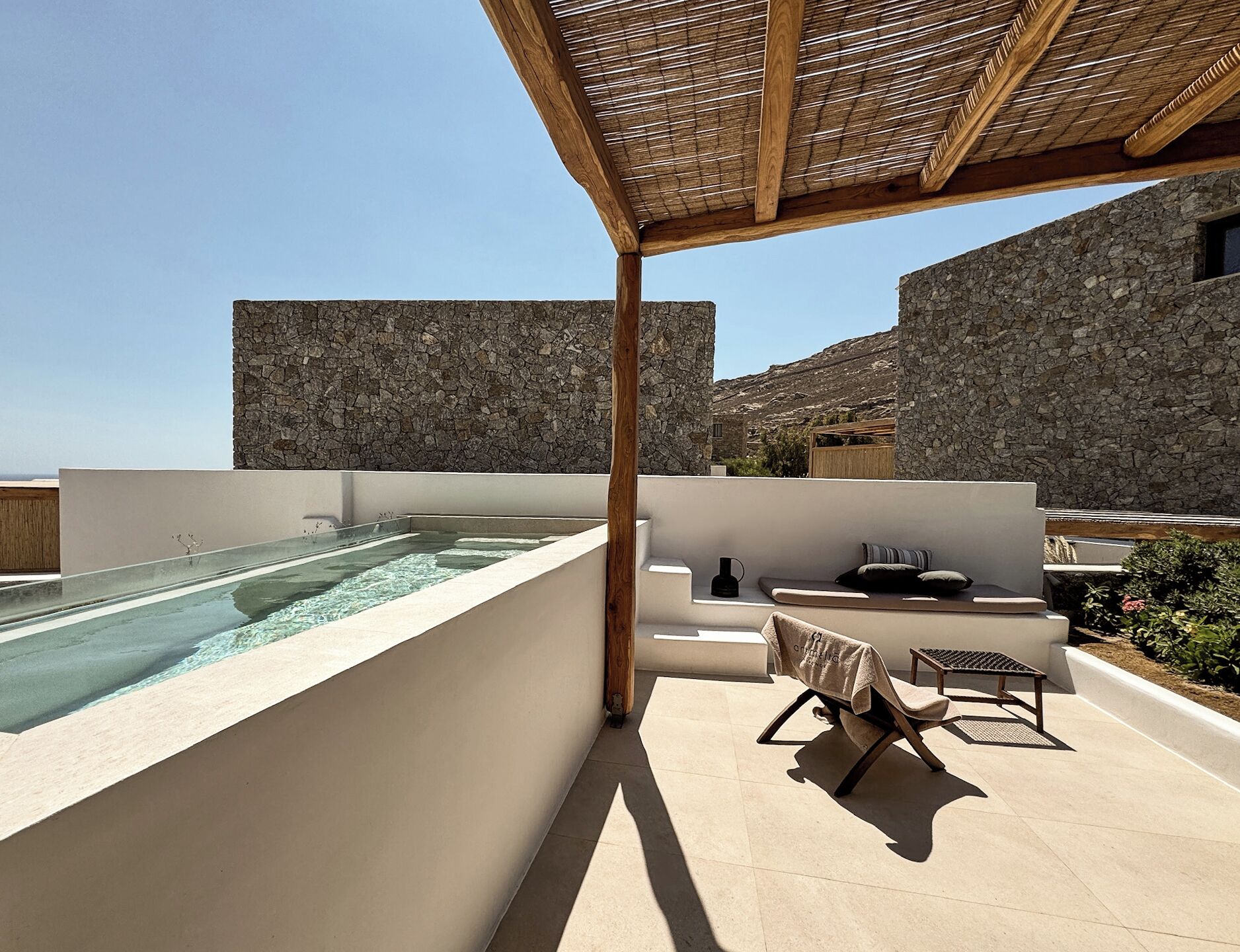 A rooftop terrace with a swimming pool, stone walls, and outdoor seating.