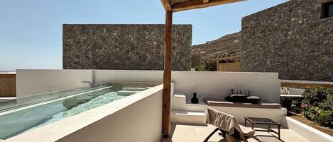 A rooftop terrace with a swimming pool, stone walls, and outdoor seating.
