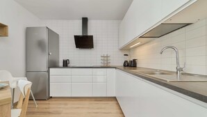 A modern kitchen with white cabinetry, a stainless steel refrigerator, a black range hood, and a sink with a modern faucet.