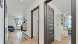 A modern apartment with a wooden floor, a grey sofa, a wooden cabinet, and a white desk with a chair.