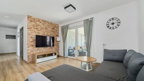 A modern living room with a brick fireplace, a flat-screen TV, a grey sofa, and a round wooden table.