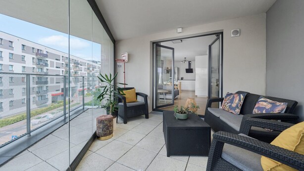 A balcony with a sofa, chairs, a small table, and a potted plant.