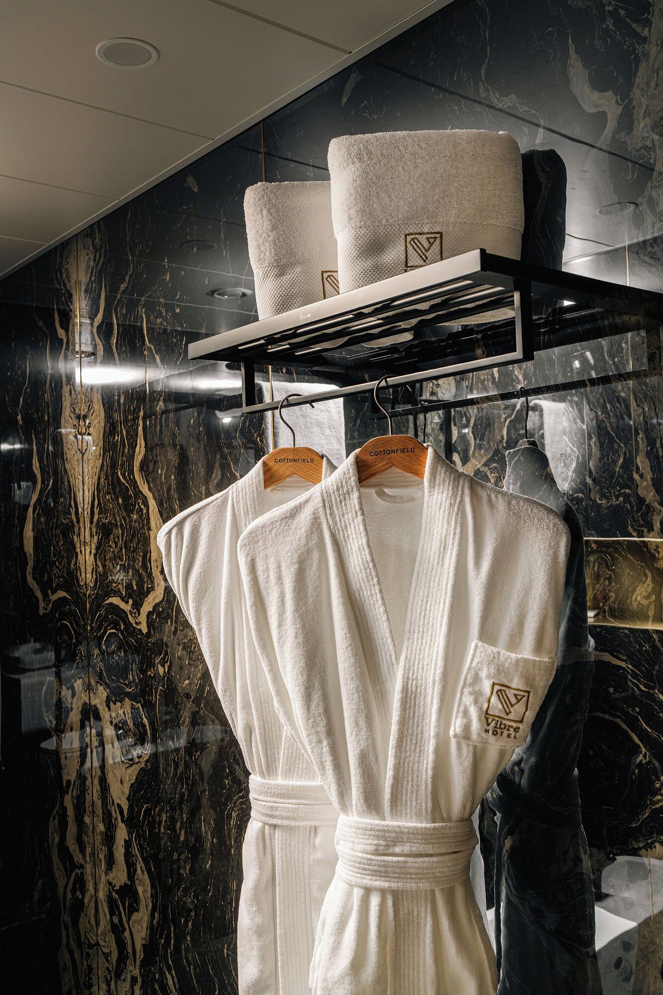 A hotel room with a marble wall, a robe rack with two robes, and a towel rack with two towels.