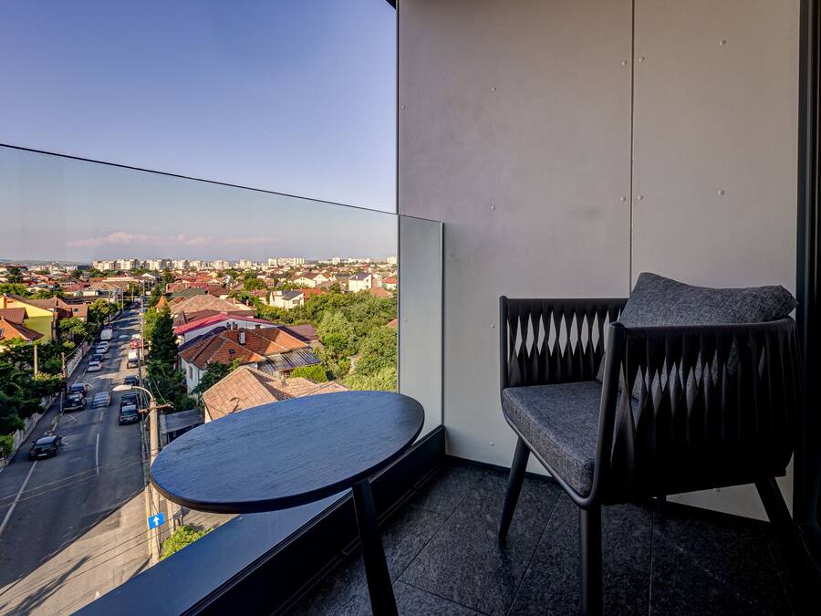 A balcony with a view of a cityscape, a round table, and a modern chair.