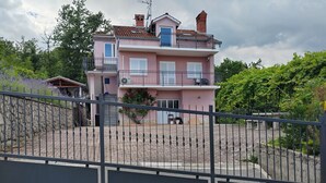 Et rosa hus med to etager, en balkon, en stenvæg og en belagt indkørsel.