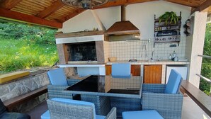 Et udendørs køkken med grill, spisebord med stole og et lille køleskab.