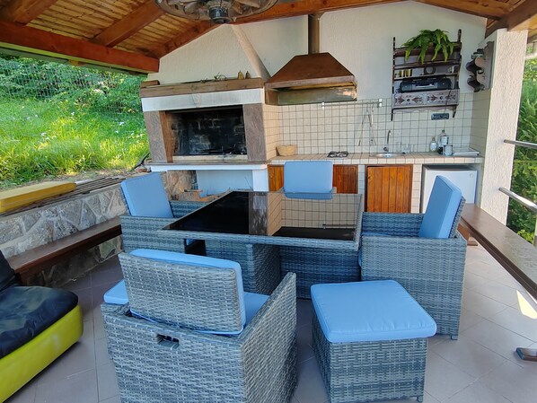 An outdoor kitchen with a grill, a dining table with chairs, and a small refrigerator.