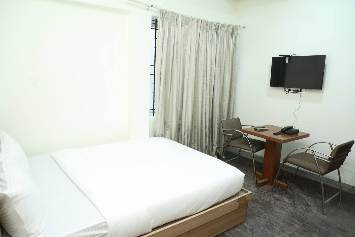 A hotel room with a bed, a desk with a chair, a television, and a window with curtains.