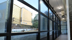 A corridor with large windows, a view of a building labeled "ASLAM PALACE," and a tiled floor. - Shoba Comfort (Bengaluru)