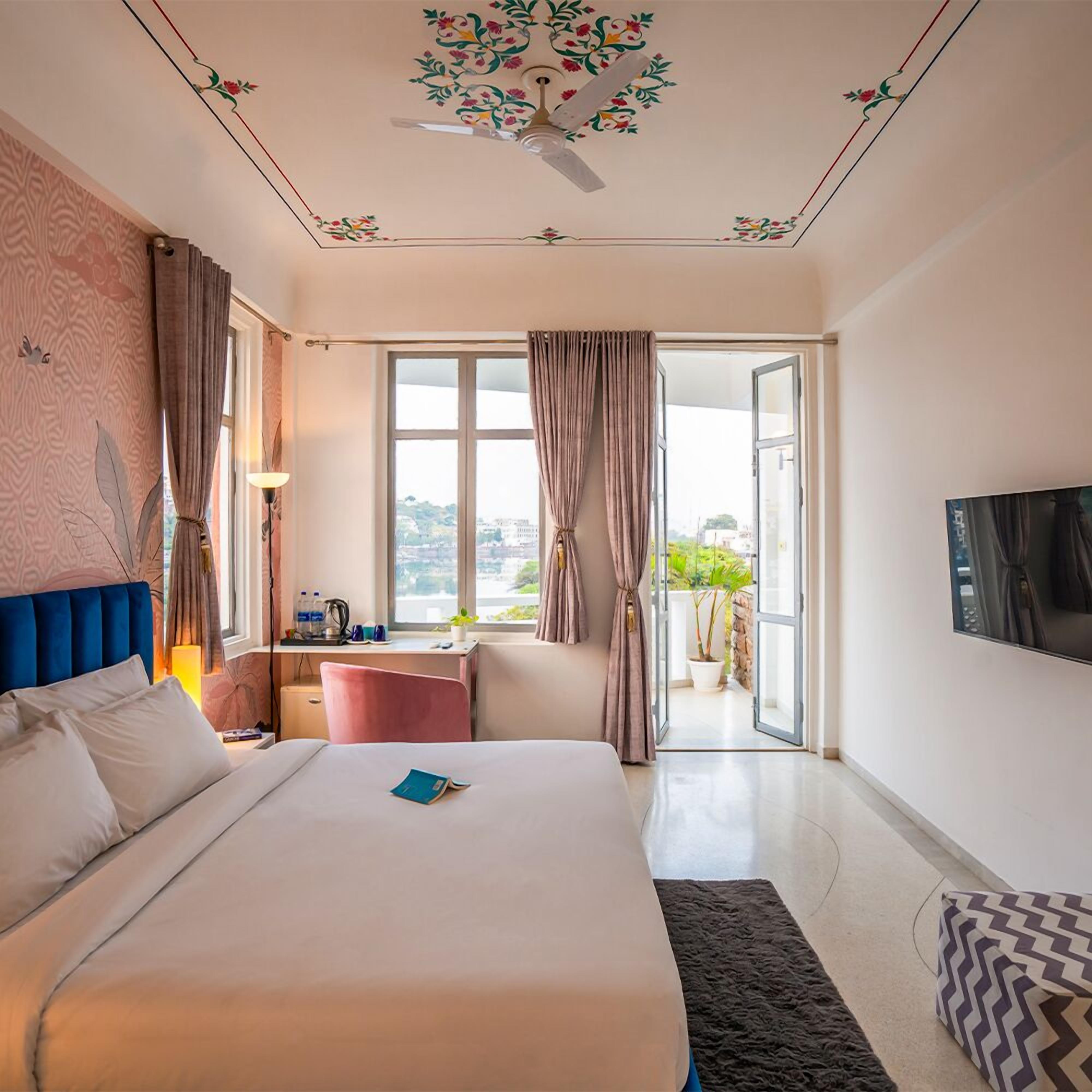 Habitación de hotel con una cama grande, un escritorio con silla, un televisor montado en la pared y vistas al exterior a través de un ventanal amplio.