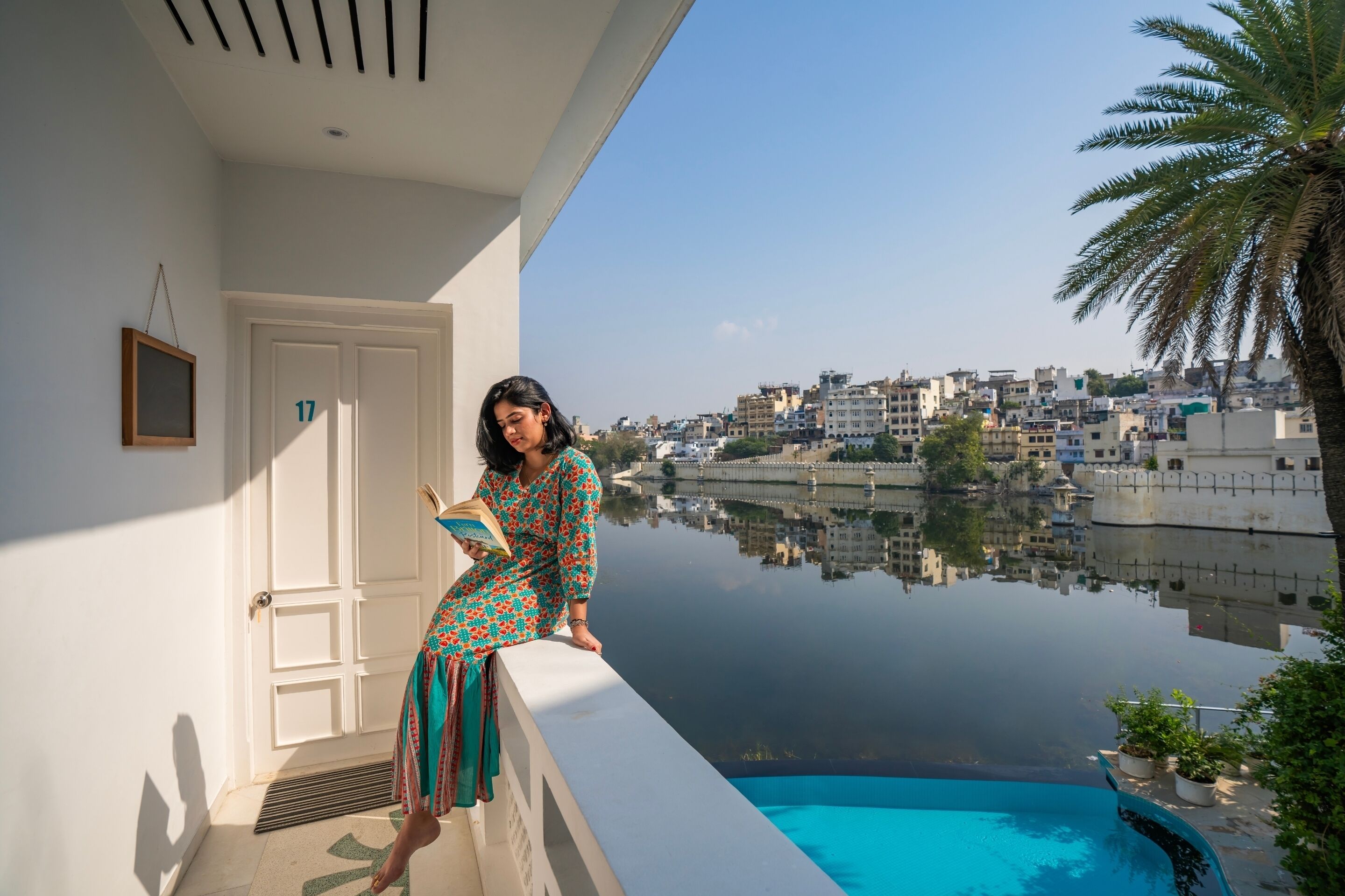 A person sitting on a balcony with a view of a cityscape and a body of water.