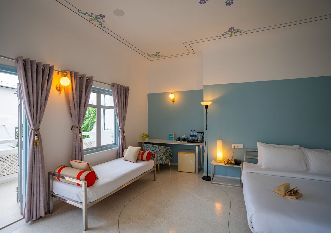 Ein Hotelzimmer mit einem Bett, einem Schreibtisch, einem kleinen Kühlschrank und einem Fenster mit Vorhängen.