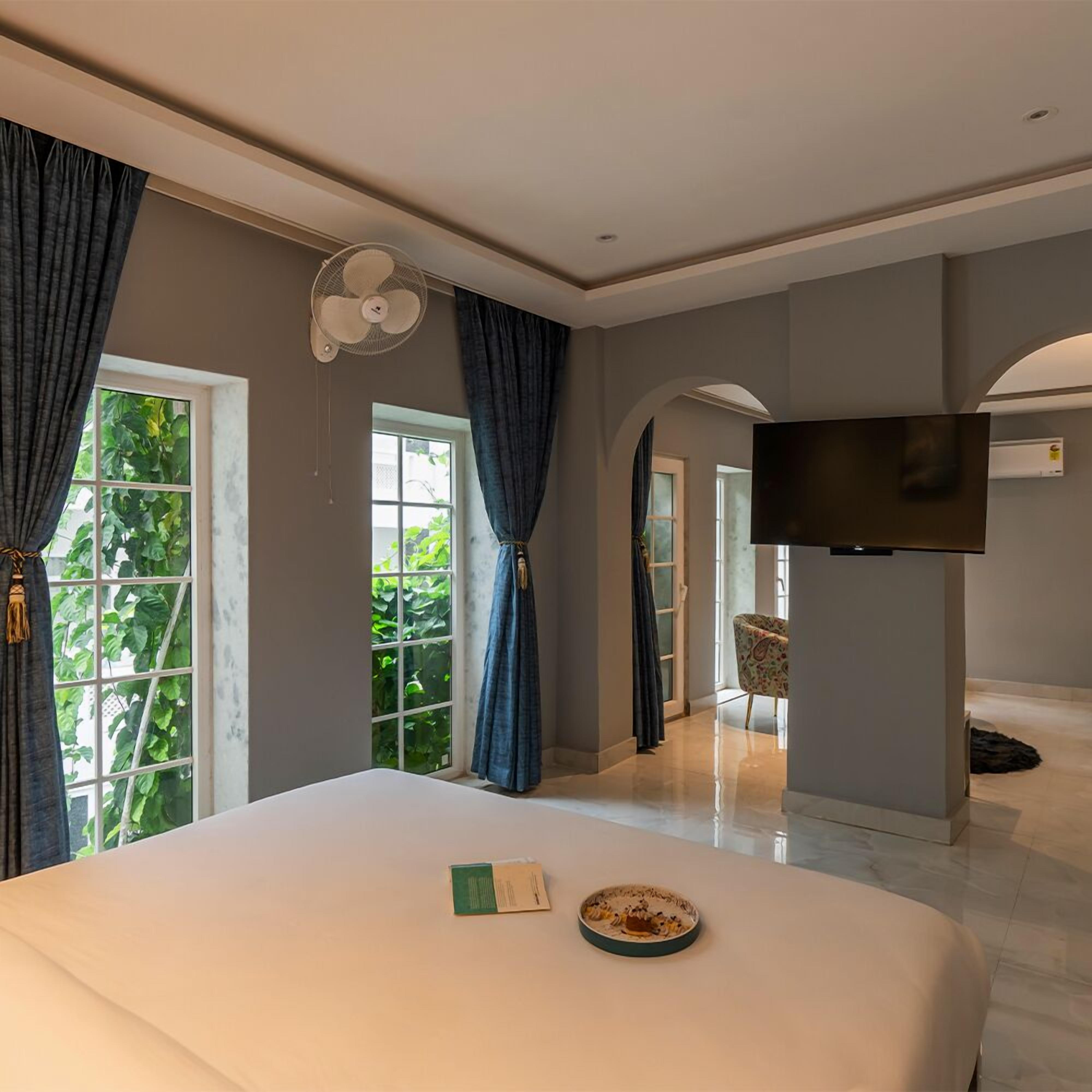 A hotel room with a large bed, a flat-screen TV mounted on the wall, and a view of greenery outside.