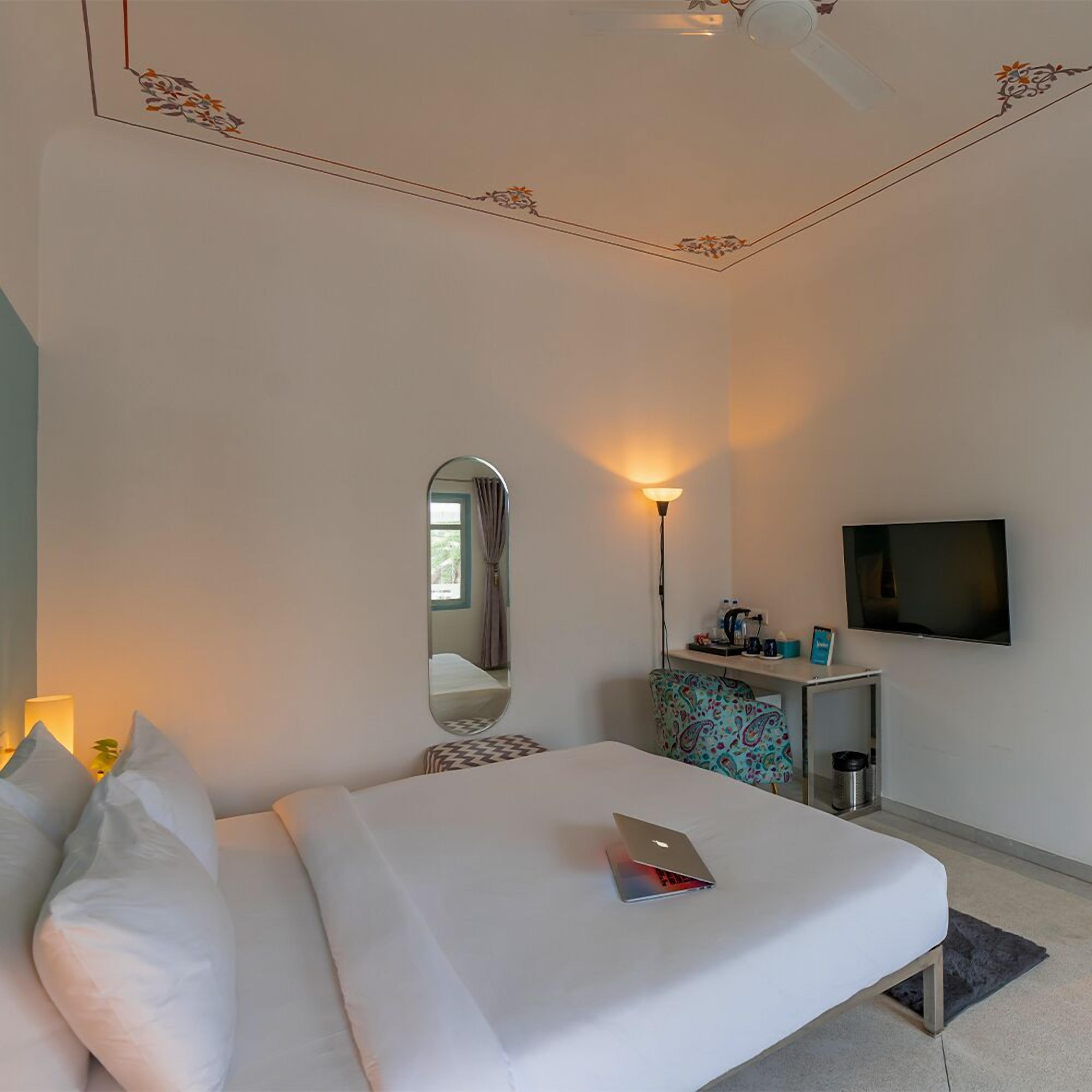 Habitación de hotel con cama, escritorio, televisor y espejo.