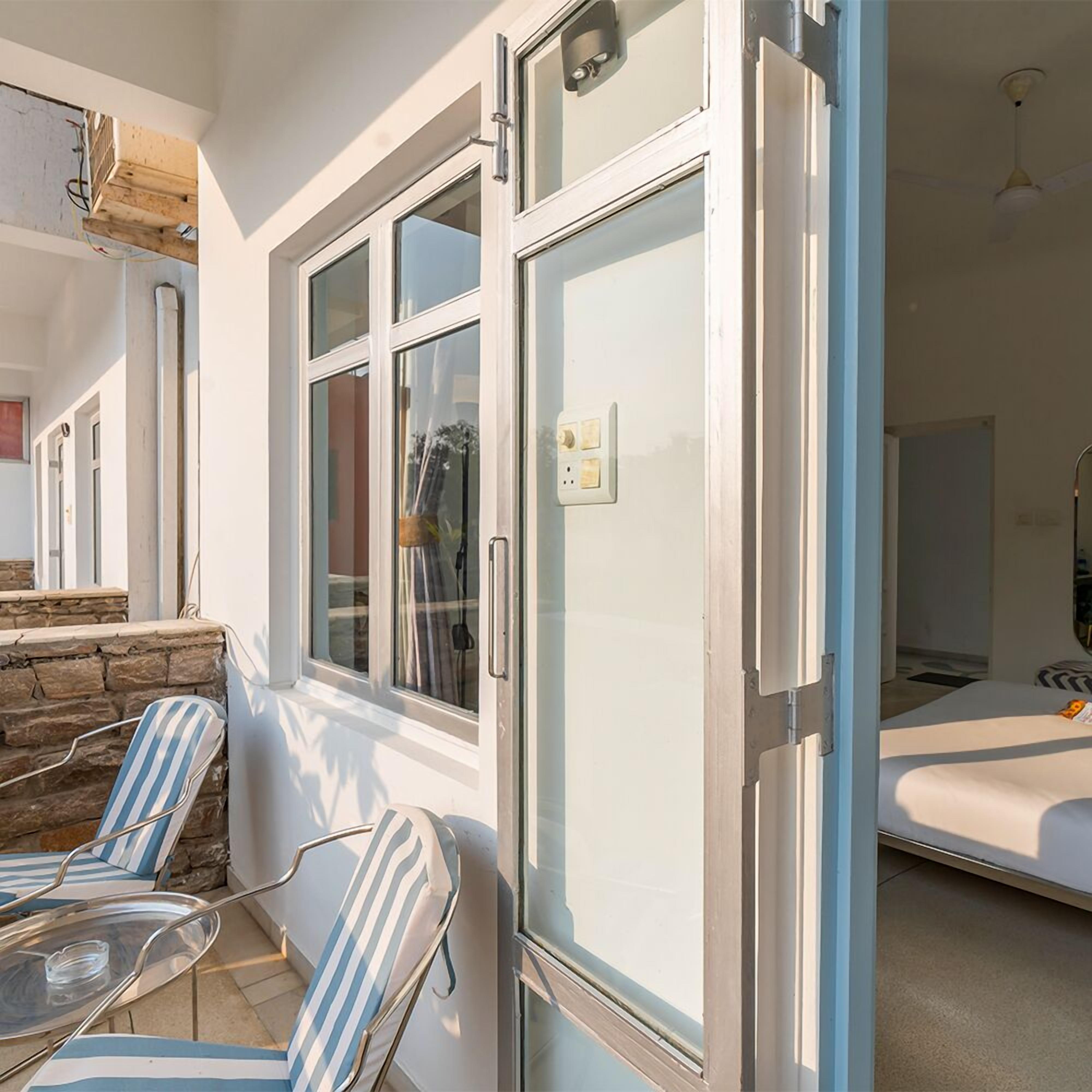 A room with a bed, a window with a curtain, and a chair with a striped cushion.
