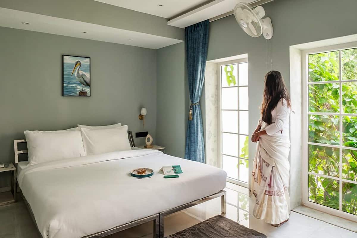A bedroom with a large bed, a bedside table, a nightstand, a window with curtains, and a ceiling fan.