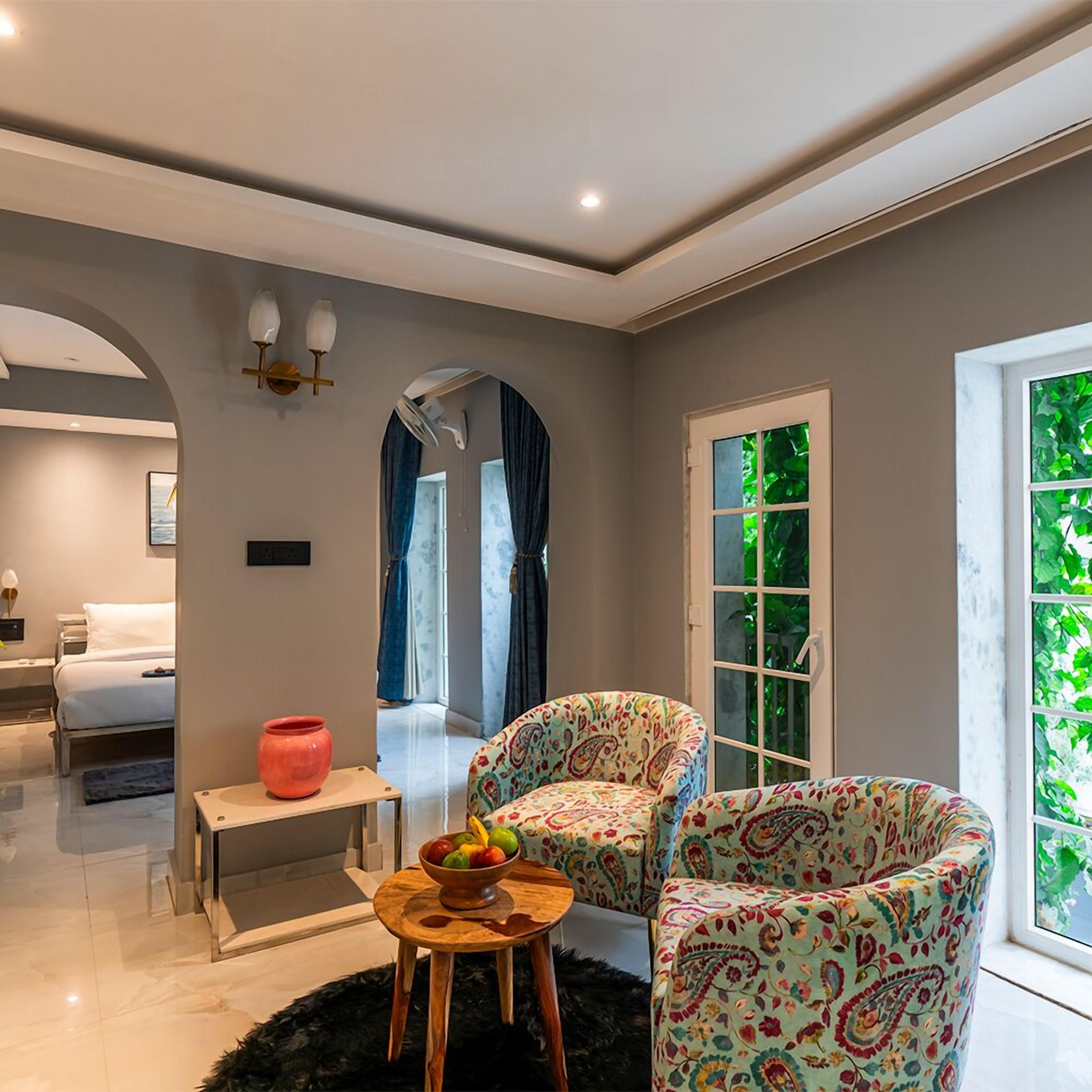 Un salon moderne avec un canapé, une petite table sur laquelle se trouve un saladier rempli de fruits, un miroir et une fenêtre donnant sur un paysage verdoyant.