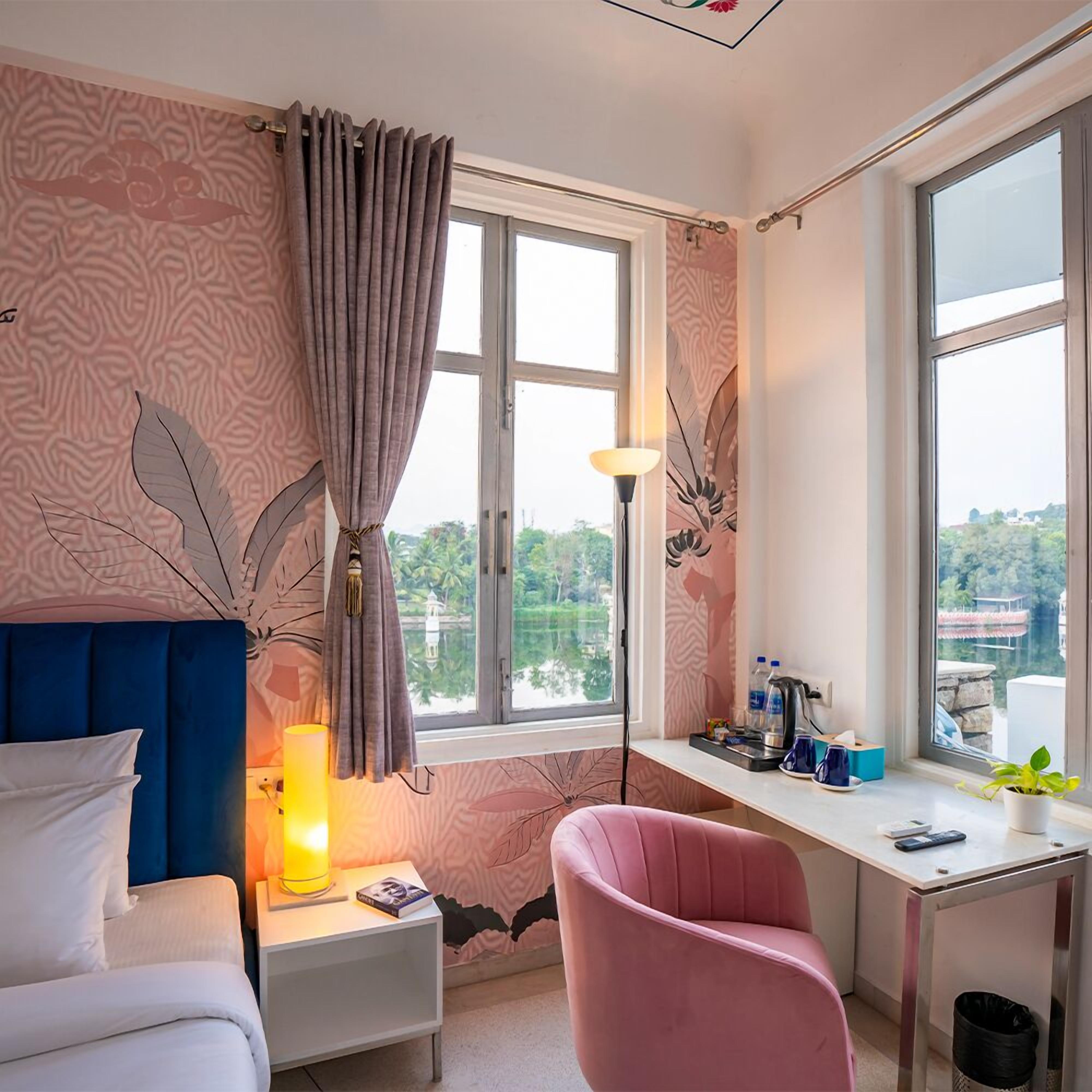 A bedroom with a bed, a desk, a chair, a lamp, and a view of the outside.