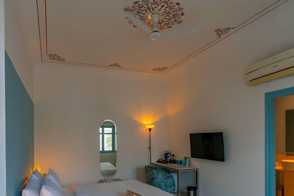 A hotel room with a bed, a desk with a lamp, a TV, and a window.