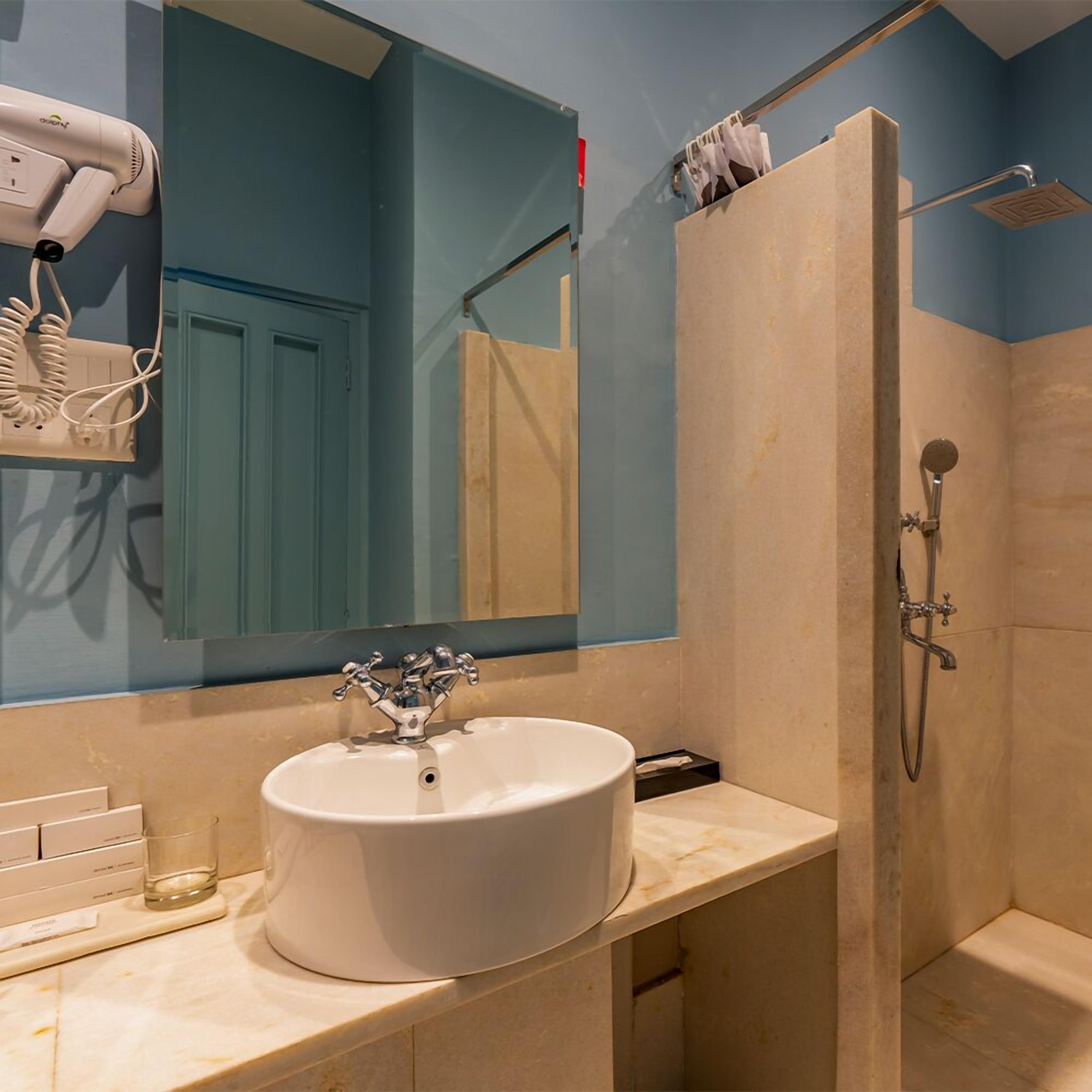 Un baño con lavamanos blanco, un espejo, secador de pelo y ducha.