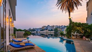 A swimming pool with lounge chairs, a palm tree, and a view of a cityscape. - Moustache Udaipur Verandah (Udaipur)
