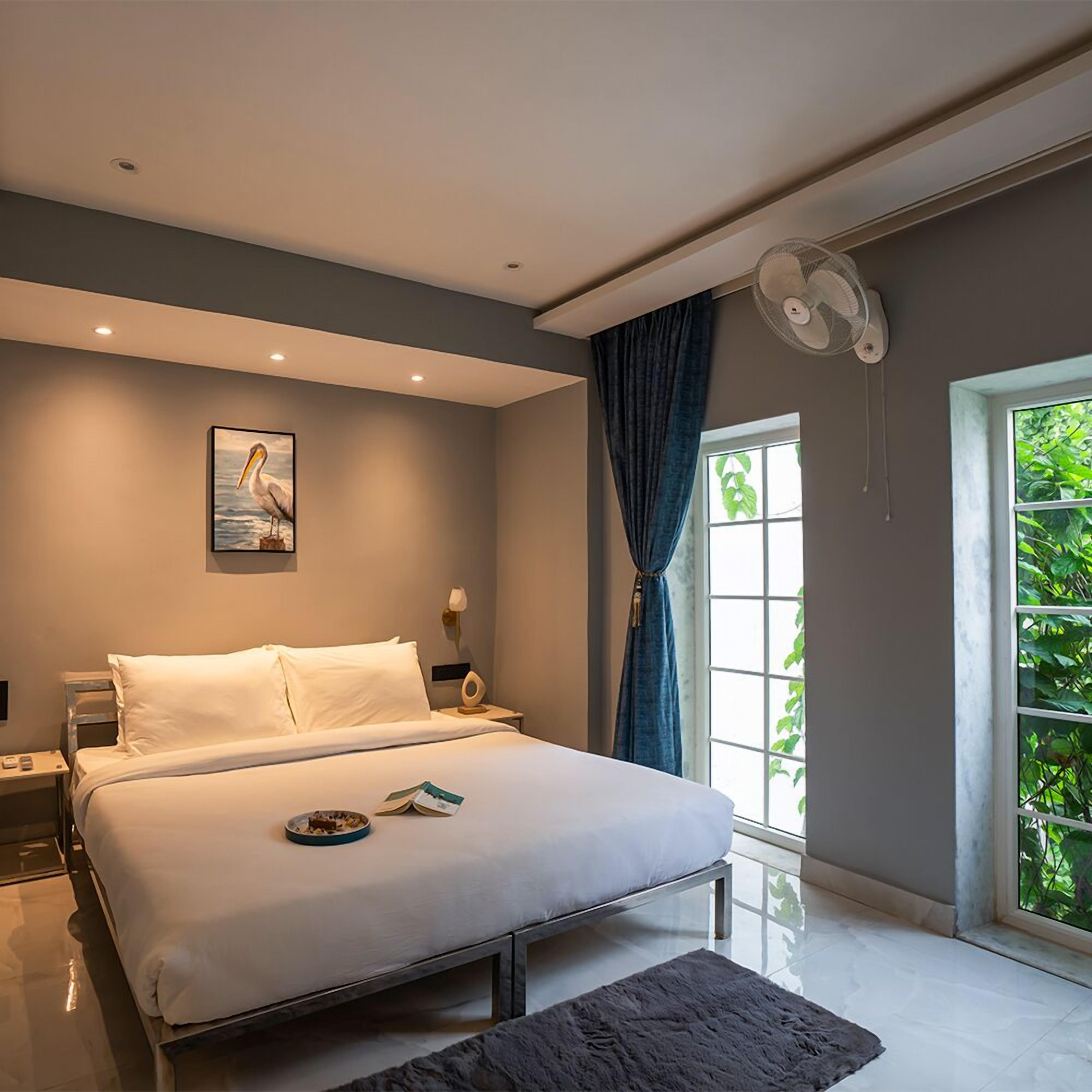 Une chambre moderne avec un grand lit, une table de chevet, une commode, une fenêtre avec des rideaux et un ventilateur de plafond.