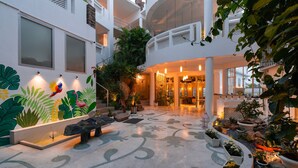 A spacious indoor courtyard with a fountain, potted plants, and a mural of tropical birds. - Moustache Udaipur Verandah (Udaipur)