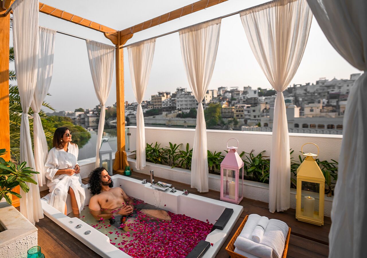 A rooftop terrace with a bathtub filled with rose petals, a wooden deck, and a city view.