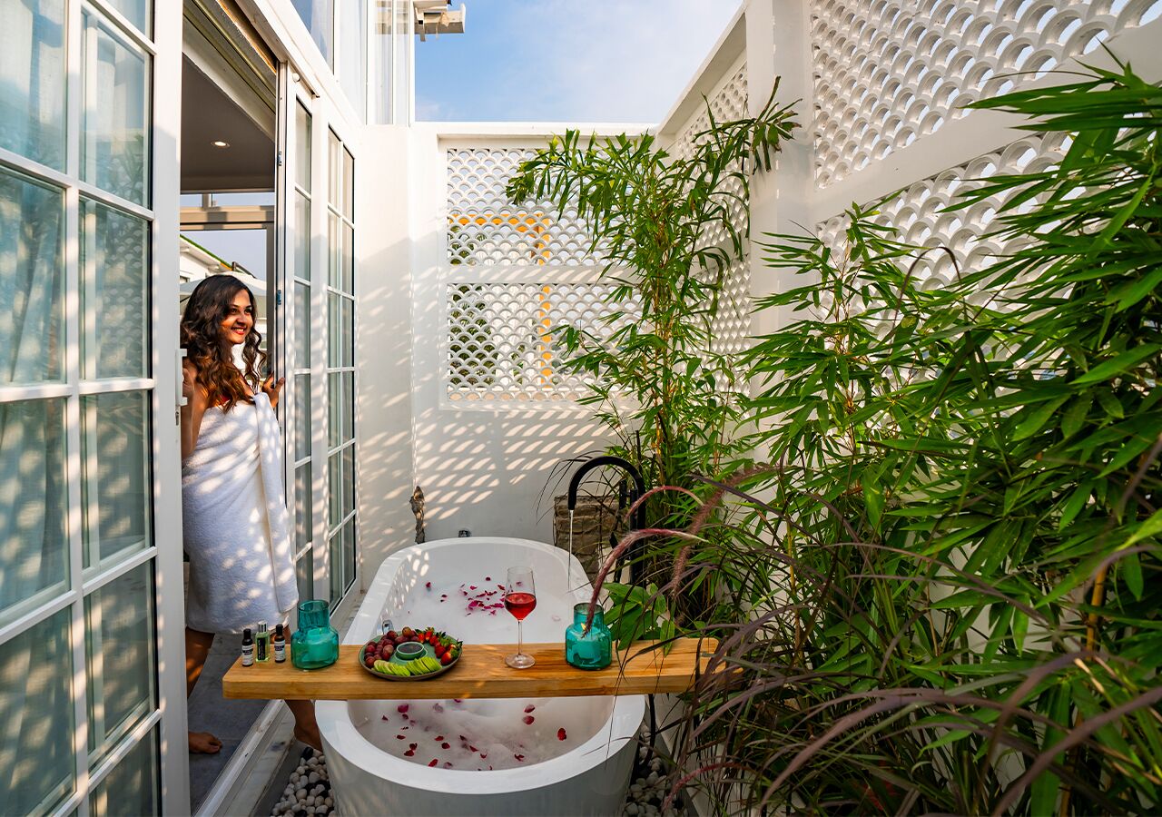 A bathroom with a bathtub, a wooden shelf with toiletries, and a bamboo plant.