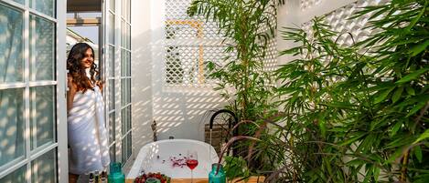 A bathroom with a bathtub, a wooden shelf with toiletries, and a bamboo plant.