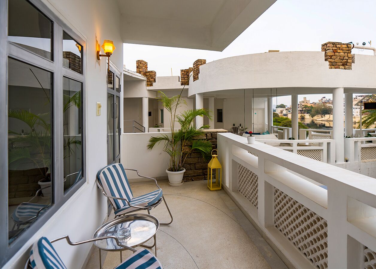 A balcony with a white railing, a potted plant, and two striped chairs.