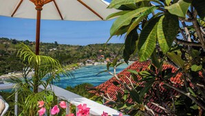 Vista de un resort tropical con piscina, abundante vegetación y una sombrilla blanca.