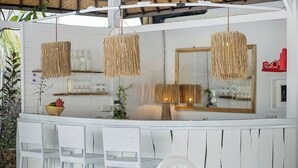 Una barra de madera blanca con sillas de mimbre, una lámpara colgante tejida y un espejo.