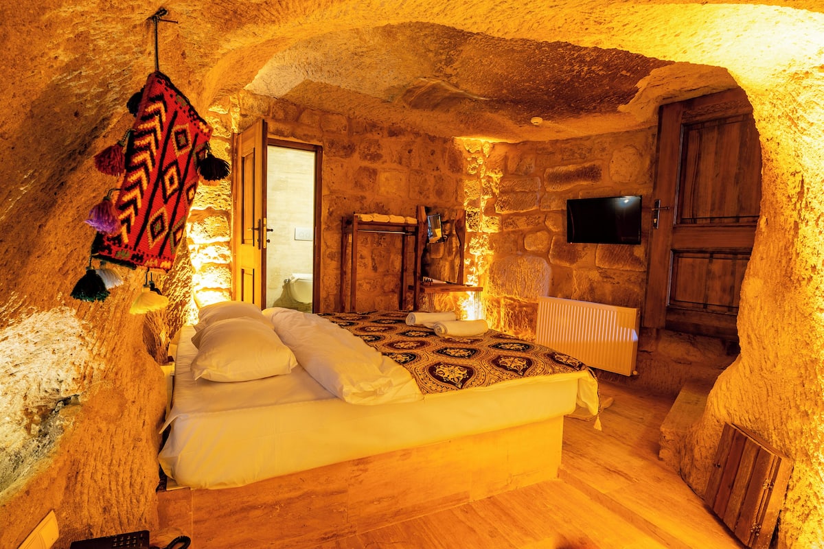 A stone-walled bedroom with a bed, wooden wardrobe, and a television.