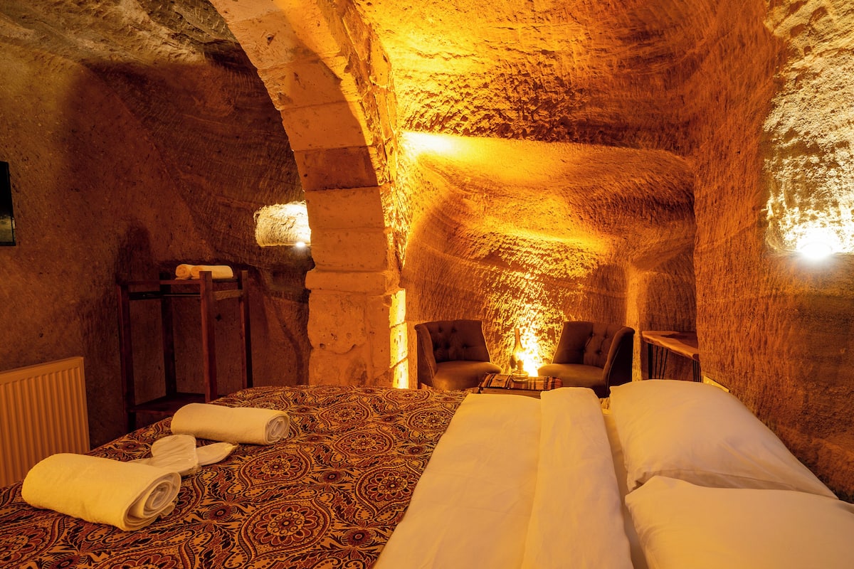 A cozy, cave-like room with a bed, two chairs, and a small table with a lamp.