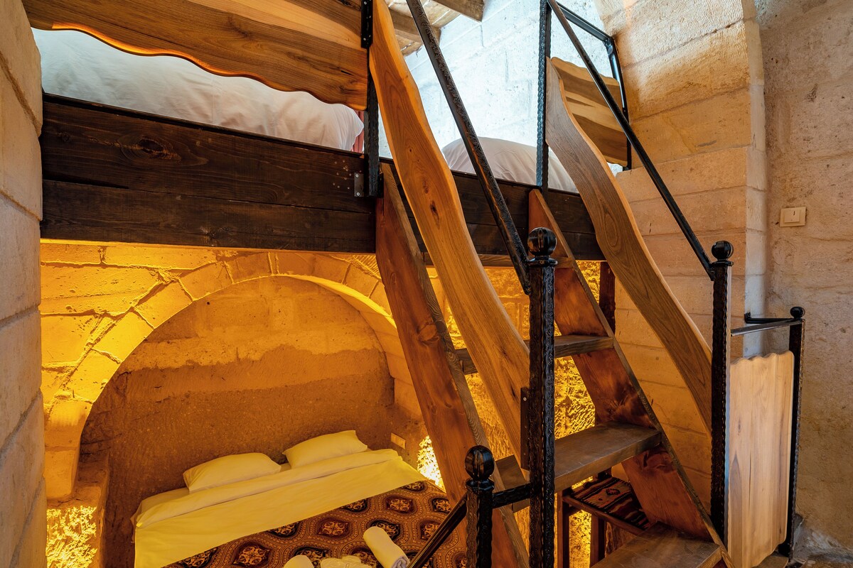 A rustic room with a wooden bed, a stone wall, and a wooden staircase.
