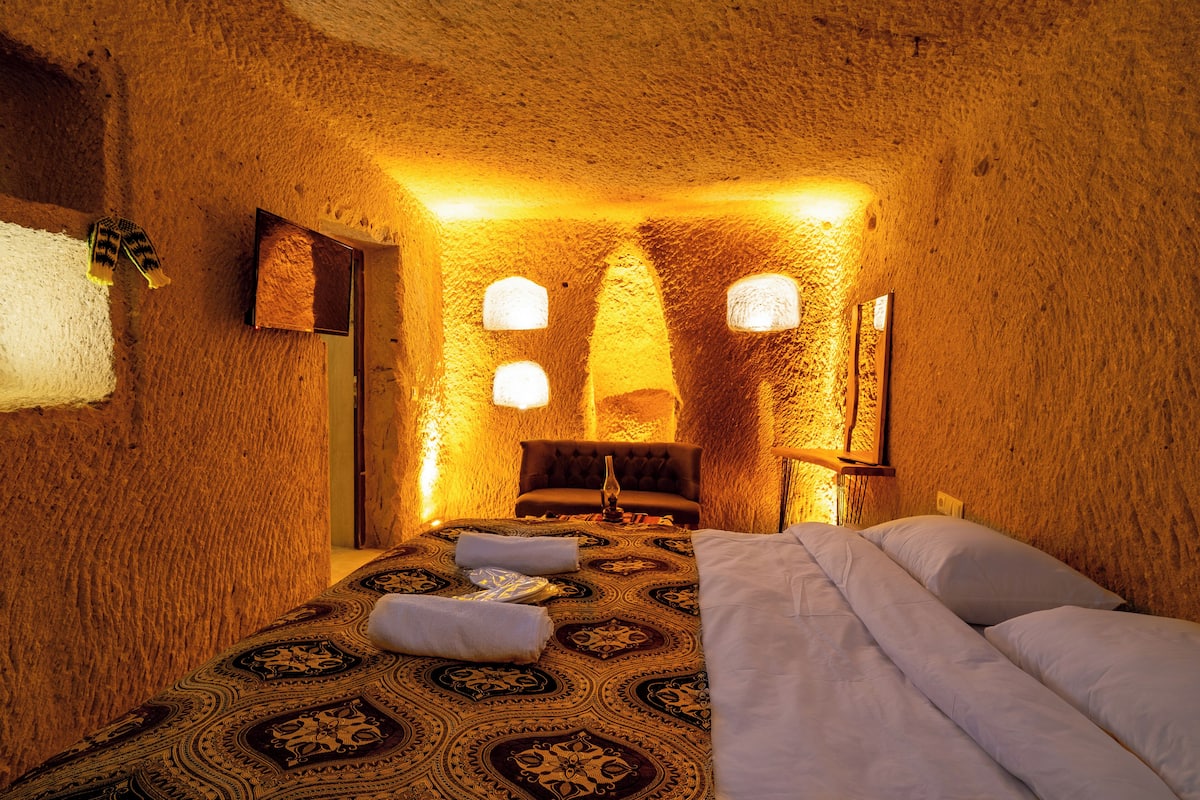 A room with a patterned carpet, a bed with white linens, and a unique textured wall.
